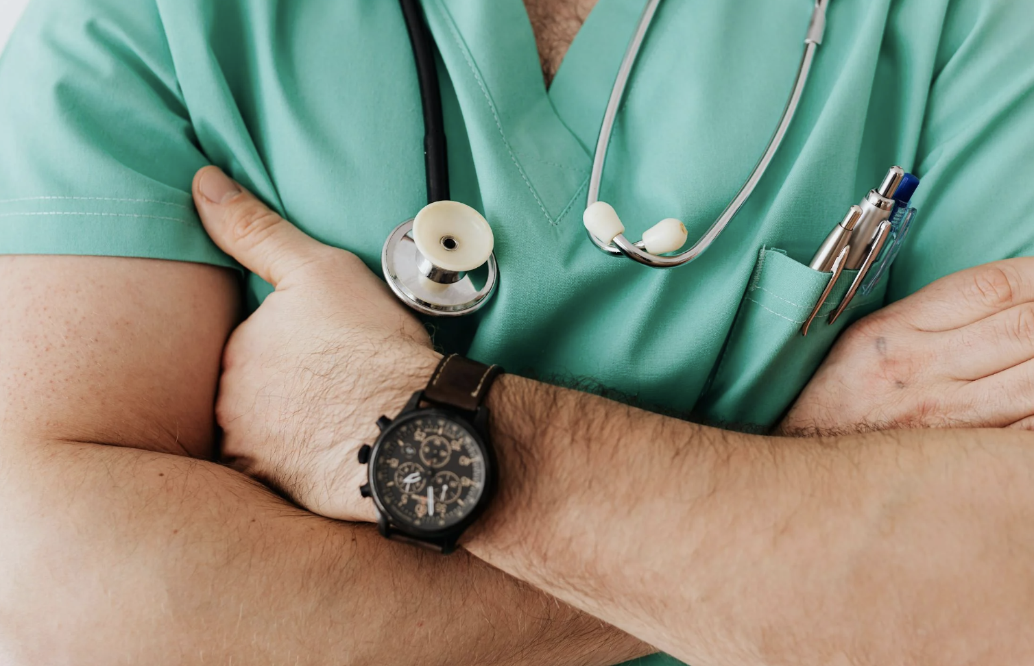 medical examiner with stethoscope around his neck and arms crossed in front of his chest.